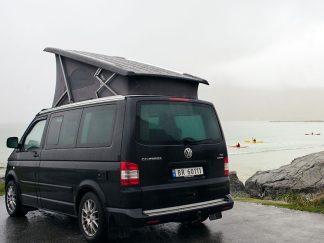 Black VW California camper with the popup roof up at the beach in Flakstad